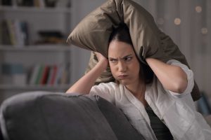 Mulher tampando os ouvidos com travesseiro enquanto bufa de nervosismo